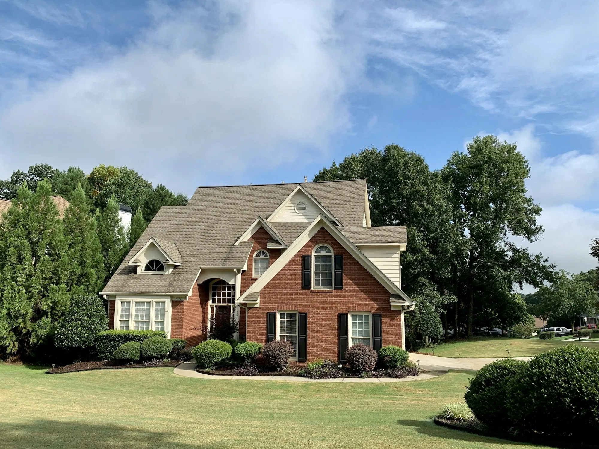 Brick two-story home with a steep architectural shingle roof and manicured lawn