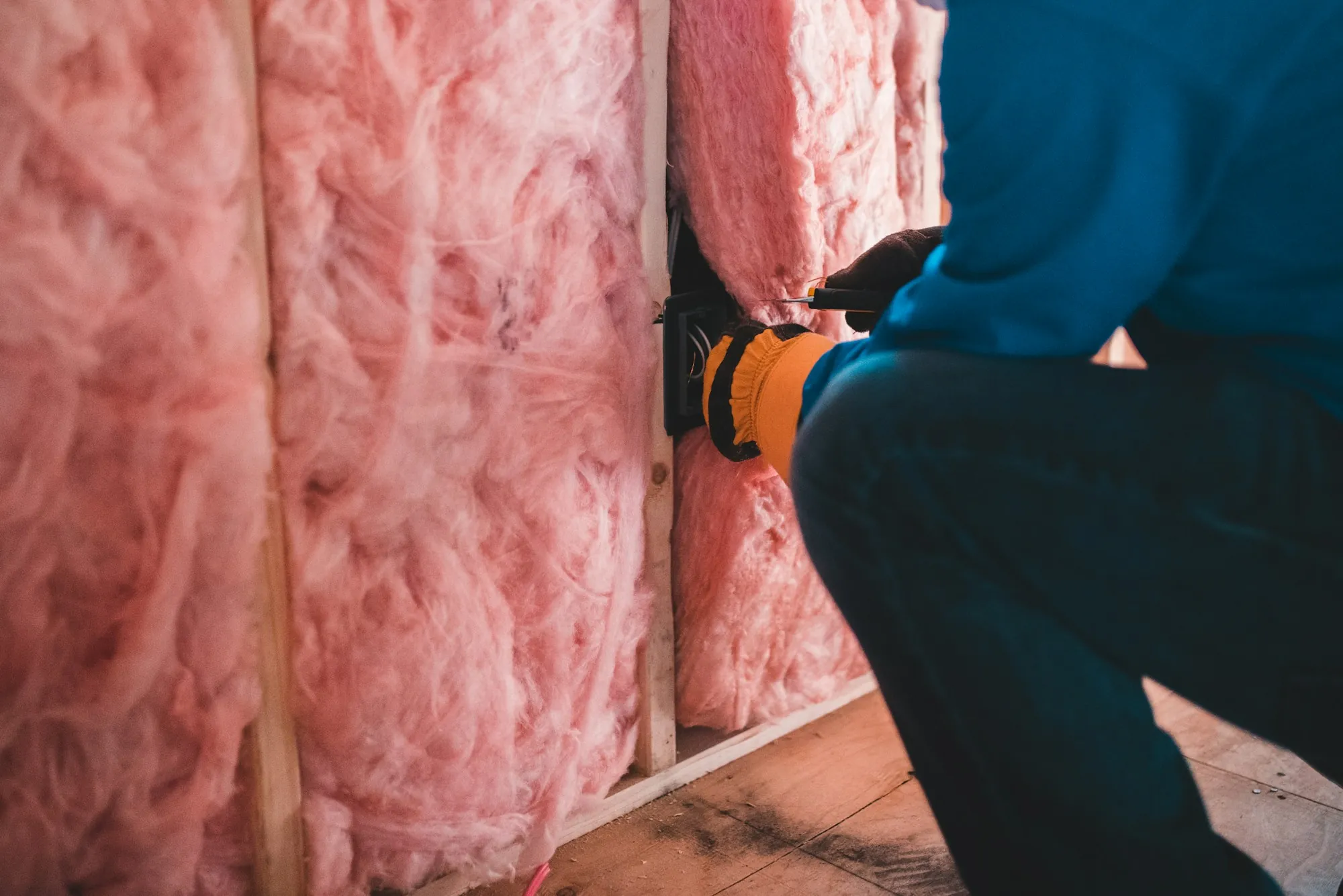 Gloved hand fitting pink insulation between wall studs