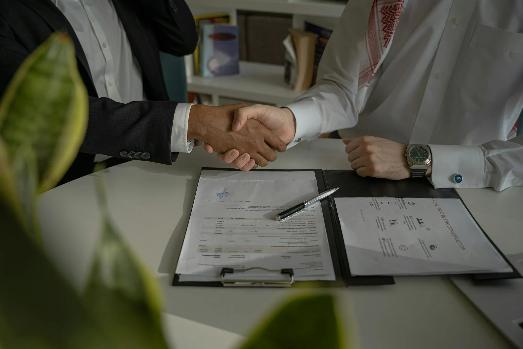 Business handshake above a signed contract on a clipboard